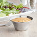 A salad with a bowl of sauce next to it in a Vollrath stainless steel sauce cup.