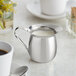 A silver stainless steel Vollrath bell creamer with a white liquid and a spoon.