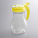 A clear polycarbonate teardrop syrup server with a yellow lid and handle.