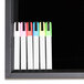 A white rectangular black marker board with black edges on a table with black and neon markers.