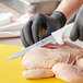 A person in black gloves using a Choice narrow flexible boning knife to cut a raw chicken.