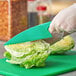 A person using a Choice plastic lettuce knife to cut a head of lettuce.