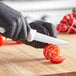 A person in black gloves using a Choice white handled utility knife to cut a tomato.