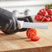 A person in black gloves using a Choice produce knife to cut a tomato.