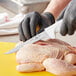 A person in gloves using a Choice 6" Narrow Semi-Flexible Boning Knife to cut chicken.