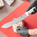 A person in gloves using a Choice 10" Butcher Knife with a white handle to cut meat on a cutting board.