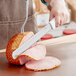 A person cutting a ham with a Choice Granton Edge Slicing Knife.