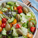 A bowl of salad with tomatoes, capers, and lettuce on a white background.