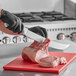 A person in black gloves using a Choice 12" Cimeter Knife to cut meat on a red cutting board.
