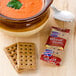 A bowl of soup next to a package of Lance Wheat Twins crackers and a spoon.