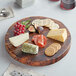 A Front of the House wooden serving board with various types of cheese and crackers on a wood surface.