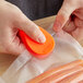 A person using an orange CrewSafe Viper bag opener to cut hot dogs on a counter.