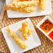 A plate of 16/20 size tempura shrimp sticks with orange and red sauce.