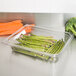 A Carlisle clear polycarbonate food pan with carrots and asparagus next to a glass dish of carrots.