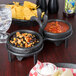 A charcoal polyethylene salsa caddy holding 2 molcajetes filled with salsa on a table with chips.