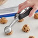 A hand using an OXO Good Grips black ice cream scoop to make a cookie.
