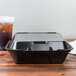 A black Genpak foam takeout container with a hinged lid and a drink inside.