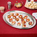A Vollrath stainless steel oval fluted tray with food on a table.