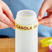 A person using a canola oil squeeze bottle with a Canola silicone label band.