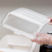 A person in gloves holding a clear plastic lid over a white container.