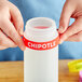 A close-up of a person's hand squeezing a Chipotle silicone label onto a bottle.