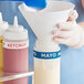 A hand in gloves pouring mayonnaise from a white bottle into a white container using a funnel with a white Choice Silicone Label Band.