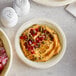 A bowl of hummus with pomegranate seeds and a white Tellus Products bagasse plate.