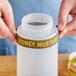 A person holding a jar of honey mustard with a silicone label band on it.