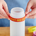 A person holding a white plastic squeeze bottle with a yellow label band that says "Sweet Red Chili"