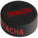 A black silicone puck with the word "Sriracha" written in red.