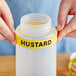 A person holding a yellow label on a mustard squeeze bottle.