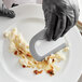 A person in a black glove using an OXO white dish squeegee to clean food on a plate.