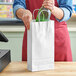 A person putting a bottle into a white Choice paper shopping bag with red trim.