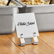 A metal deli tag pan sign holder clip on a table with a sign that says "potato salad"
