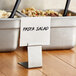A white container with a black Choice stainless steel deli tag holder on a table in a salad bar.