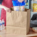 A person putting a bag of popcorn into a brown Kraft paper bag with handles.