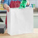 A woman putting a bottle of soda into a white paper shopping bag.
