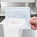 A hand using a Cambro translucent plastic lid to cover a plastic container.