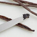 A knife cutting into a Madagascar Bourbon vanilla bean on a table.