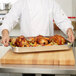 A chef holding a Vollrath Wear-Ever aluminum roasting pan of chicken and vegetables.