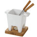 A white Boska ceramic fondue pot with wooden handles and two fondue forks.