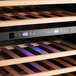 An AvaValley dual temperature wine cooler with blue lights on a wooden wine rack.