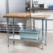 An Advance Tabco stainless steel work table with a galvanized undershelf and a wooden cutting board.
