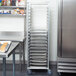 A Cres Cor sheet pan rack filled with metal sheet pans in a school kitchen.