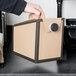 A person's hand holding a brown and black Sabert Beverage on the Move take out container box.