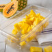 A glass food pan with pineapple and papaya slices in it.