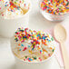 A bowl of ice cream with rainbow sprinkles next to a spoon.
