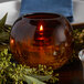 A Sterno amber glass sphere candle holder with a crackle base holding a lit candle on a table with a plate of food.