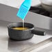 A black Valor mini cast iron fondue pot with yellow liquid inside being stirred with a blue brush.