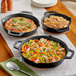 Three Valor pre-seasoned cast iron skillets on a table with food in them.